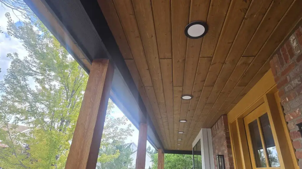 Prefinished Woodtone tongue and groove porch ceiling with black beam and wood columns on a Highlands Ranch, Colorado home